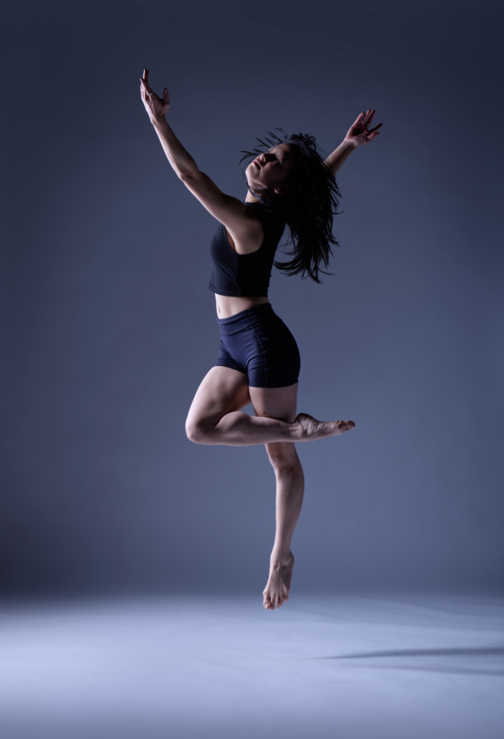 Female dancer in a black biketard with long loose hair jumping with one foot raised, credit Leon Glory Damasco Jr