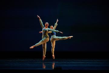 2 female dancers in teal leotards and leggings in split jumps