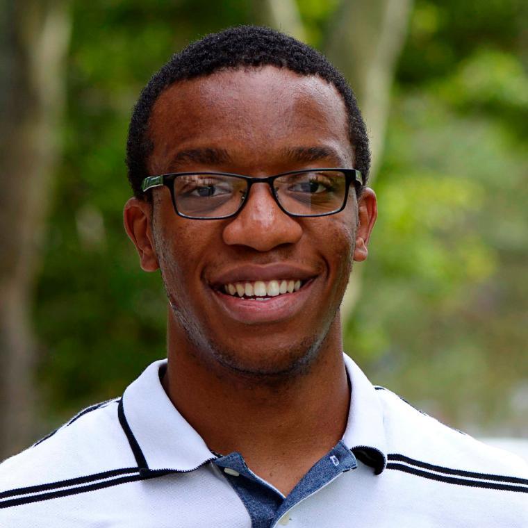 A person smiling with glasses and a polo shirt, outdoors.