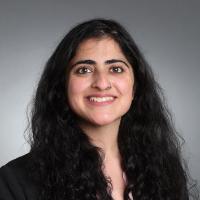 A person in professional attire smiling against a gray background.