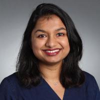 A person smiling in a professional headshot with a grey background.