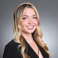 A woman with a smile dressed in business attire against a gray background 