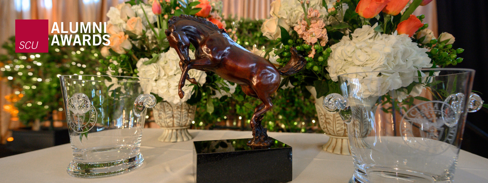 Alumni Awards Jumbotron trophy surrounded by flowers and glasses.