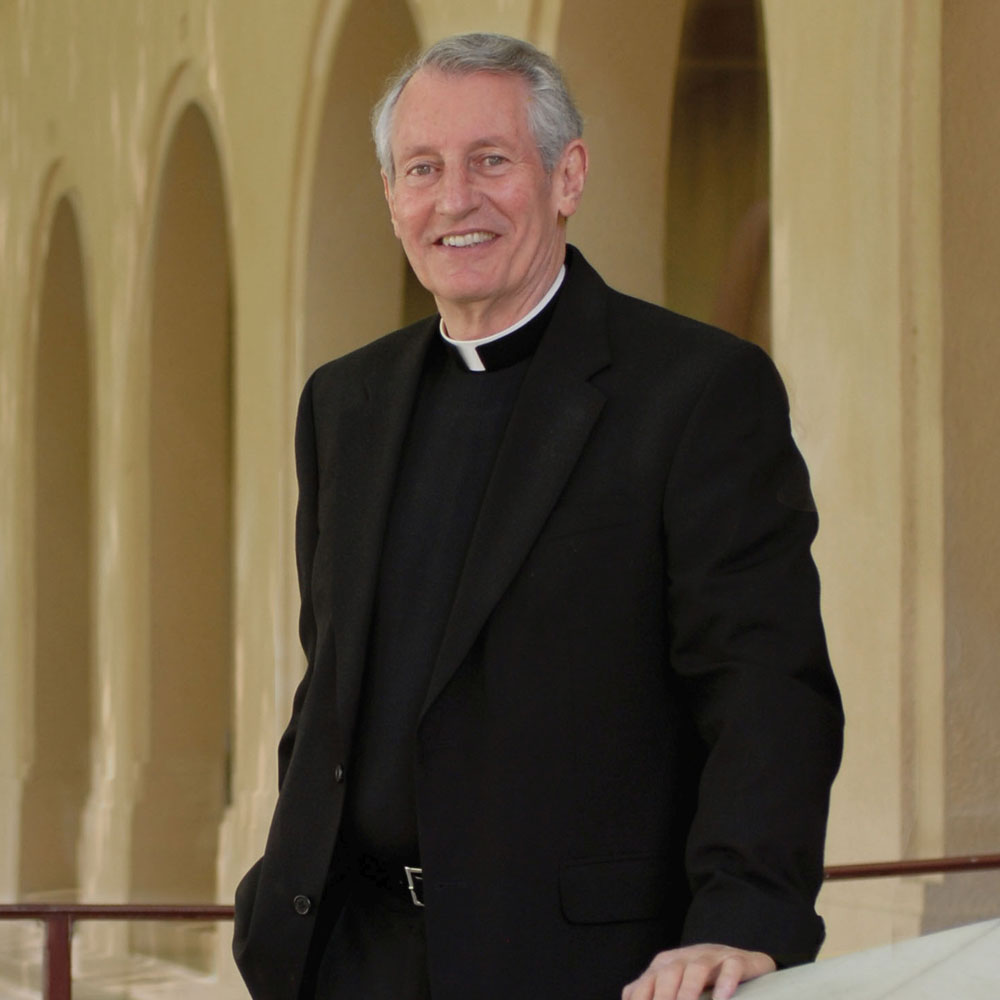 A priest stands in front of pillars on a college campus