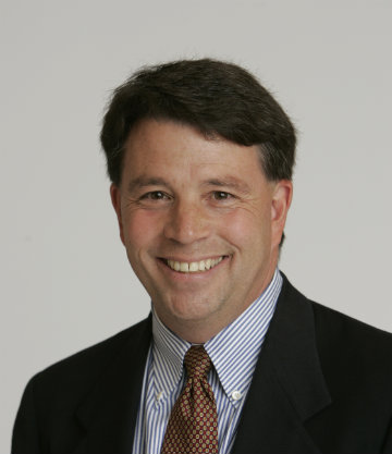A person smiling in formal attire against a plain background.