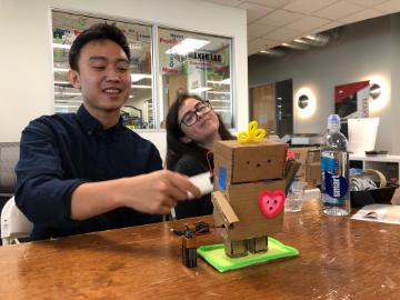 Two people smiling and interacting with a craft project on a table.
